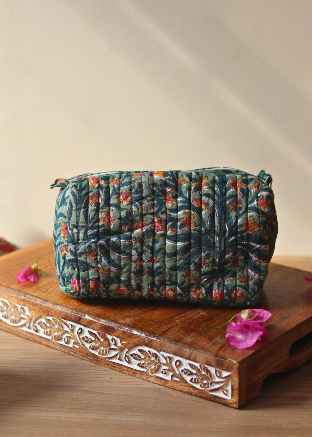 Green toiletry bag on wooden tray with flowers