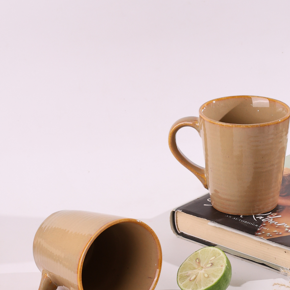 Two cream coffee mugs one is laying one is standing on a book