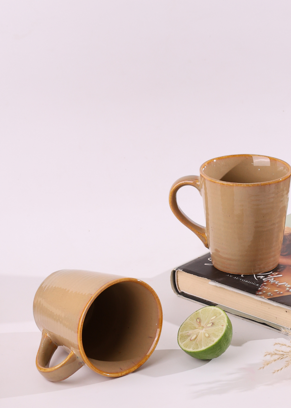 Two cream coffee mugs one is laying one is standing on a book