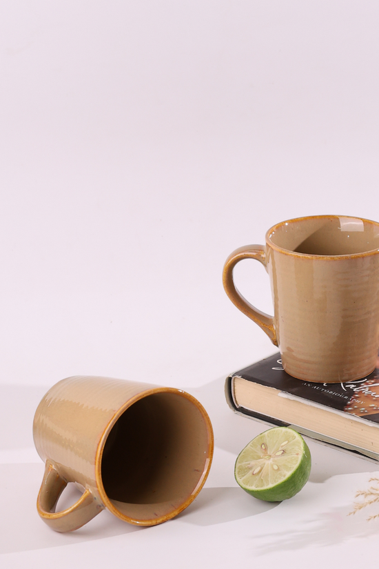 Two cream coffee mugs one is laying one is standing on a book