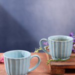 Two sky blue cups one having tea on a wooden surface