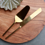 Gold cake cutter & server on wooden surface