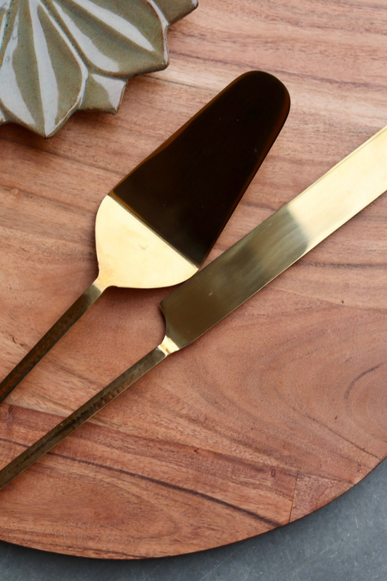 Gold cake cutter & server on wooden surface