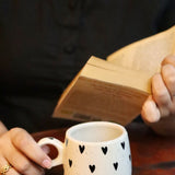 someone is holding a black heart mug and a book on hand