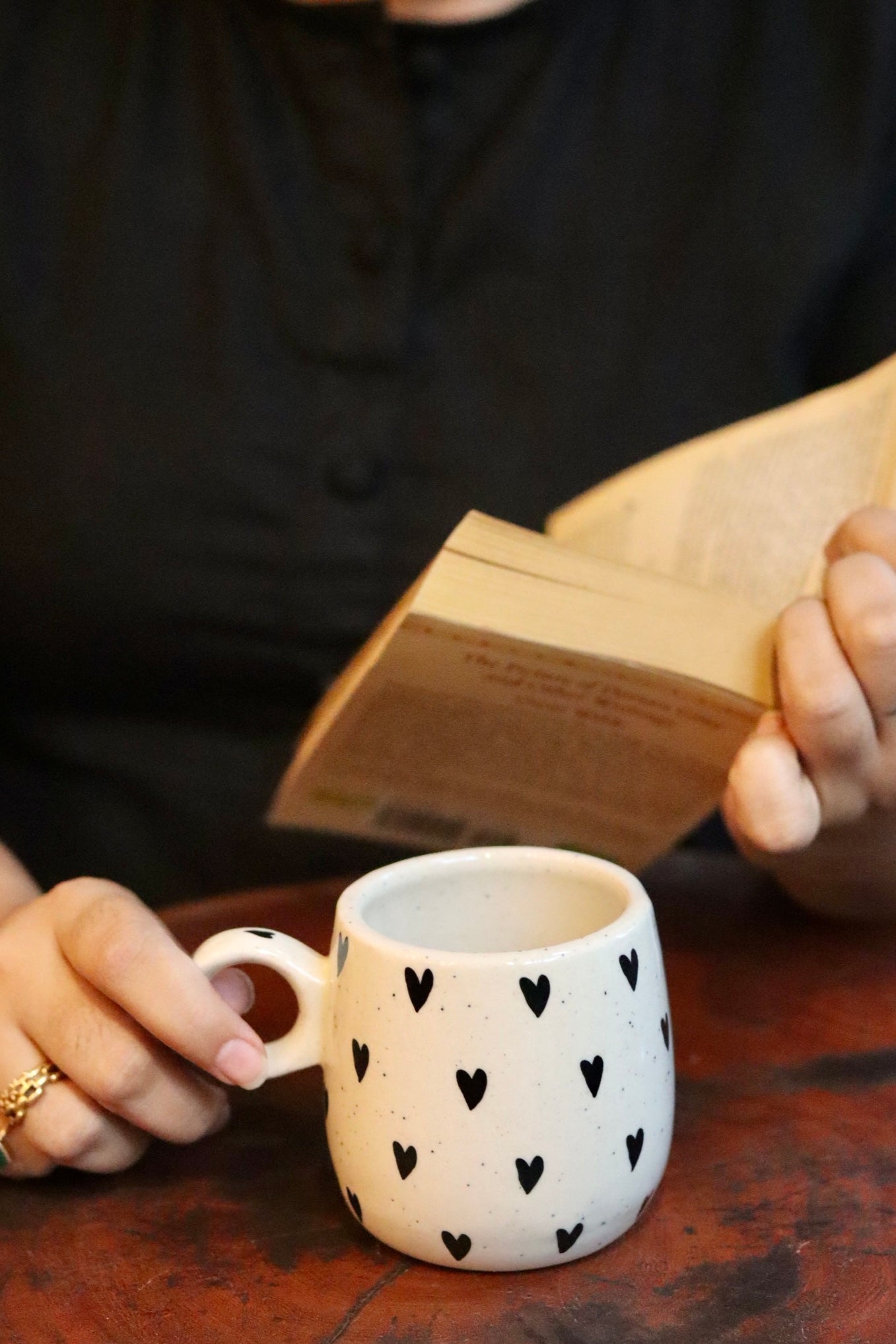 someone is holding a black heart mug and a book on hand