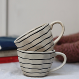 Two black lined handmade coffee mugs on each other